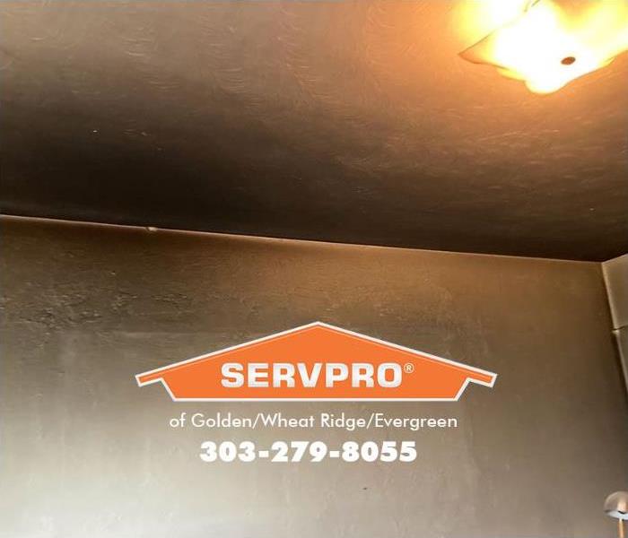 A SERVPRO Technician is cleaning smoke and soot residue from the ceiling and walls in a fire-damaged house. 